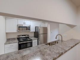Spacious renovated kitchen at Huntley Ridge East with stainless steel appliances, white cabinets, granite-style countertops, and a breakfast bar overlooking the dining area.