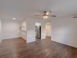 Bright open-concept living space at Huntley Ridge East with wood-style flooring, ceiling fan, neutral walls, and easy flow into the kitchen area.