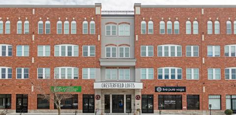 Chesterfield Lofts A wide shot of Chesterfield Lofts, highlighting its symmetrical brick architecture with large windows and decorative detailing. The ground floor features multiple businesses, including a yoga studio and wellness center, with additional commercial spaces available for lease. The entrance is centrally located, flanked by retail spaces designed for high foot traffic.
