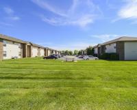 Expansive green lawn between two rows of apartment buildings at Huntley Ridge East in Springfield, MO, with a picnic table and resident parking under a bright blue sky.